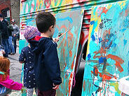 A couple of young kids in front of two panels as tall as them, painting bright and abstracted colorful patterns.